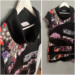 Puede incluir: Camiseta negra de manga corta con cuello alto y estampado abstracto de colores. La camiseta tiene una etiqueta que dice "Infinites".