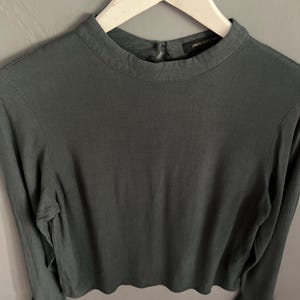 May include: A long-sleeved, dark teal top with a high neckline and flared cuffs. The top is hanging on a white hanger. The tag reads "Urban Outfitters".