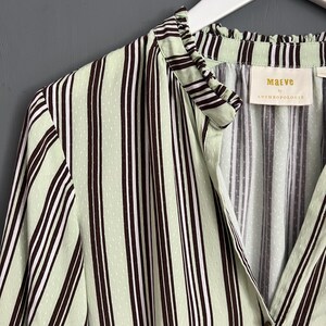 May include: A green and brown striped shirt with a ruffled collar and a button closure. The shirt has a small white tag with the text "Maeve by Anthropologie" on it.