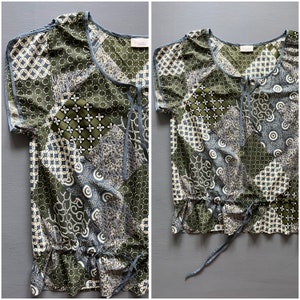 Op de afbeelding: Een groen en blauw gebloemd blouse met korte mouwen en een trekkoord aan de onderkant. De blouse heeft een ronde hals en een strik aan de hals.