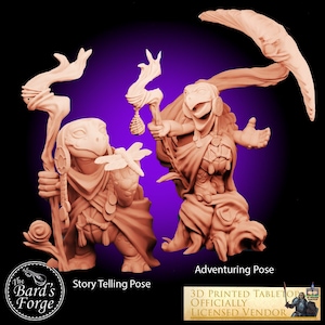 May include: Two 3D printed miniature turtle figures in different poses. The turtle on the left is holding a staff and a dragonfly, while the turtle on the right is holding a staff and has a flowing robe. Both figures are painted in a light brown colour.