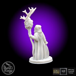 May include: White 3D printed miniature of a wizard holding a staff with a deer skull and antlers at the top. The wizard is wearing a hooded robe and is standing on a round base.