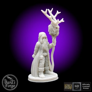 May include: White 3D printed miniature of a Santa Claus figure holding a staff with a deer skull on top. The figure is wearing a long coat and boots. The miniature is on a round base.