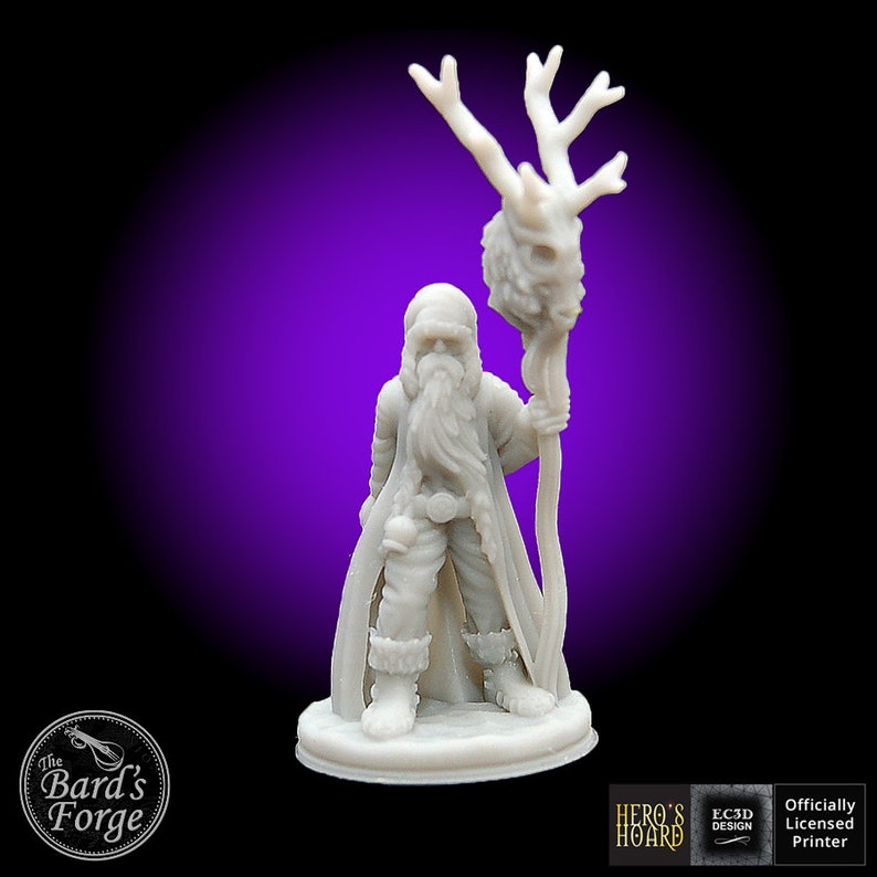 May include: A white 3D printed miniature of a bearded figure wearing a hooded robe and holding a staff with a skull and antlers. The figure is standing on a round base. The miniature is part of a set of fantasy role-playing game characters.