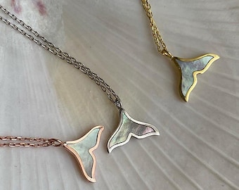 May include: Three necklaces featuring whale tail pendants with iridescent mother-of-pearl inlays. One pendant is set in rose gold, one in silver, and one in gold, each attached to a matching delicate metal chain link necklace.