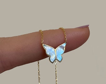 Pode incluir: Um colar de corrente dourada com um pingente de borboleta com incrustação de madrepérola branca iridescente. As asas da borboleta são contornadas em ouro e a corrente delicada conecta-se ao topo do pingente, criando uma peça de joalharia refinada.