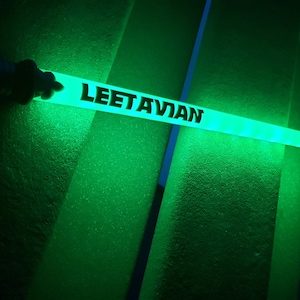 Puede incluir: Un palo luminoso verde con el texto "LEETAVIAN" impreso en &eacute;l.