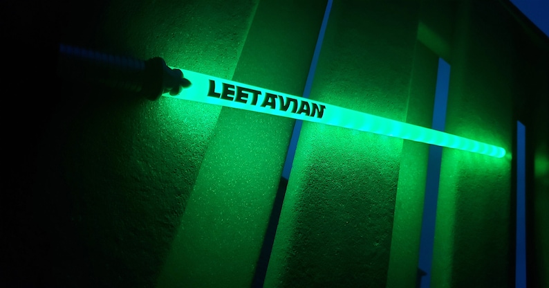 Puede incluir: Un palo luminoso verde con el texto "LEETAVIAN" impreso en &eacute;l.