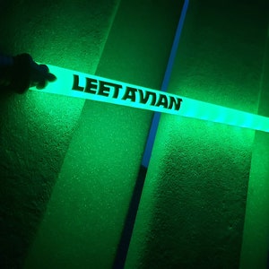 Peut inclure: Un b&acirc;ton lumineux vert avec le texte "LEETAVIAN" imprim&eacute; dessus.
