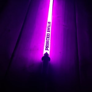 Puede incluir: Un palo luminoso morado con el texto "Princess Emilia" impreso en &eacute;l.