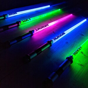 Puede incluir: Cinco espadas de juguete luminosas de colores con nombres escritos en ellas: Bree, Lucy, Lauren, Maddie y Mikey.
