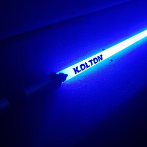 Peut inclure: Un b&acirc;ton lumineux bleu avec le nom "KOLTON" imprim&eacute; dessus.