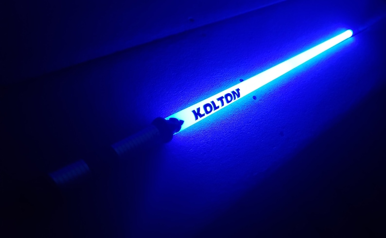 Peut inclure: Un b&acirc;ton lumineux bleu avec le nom "KOLTON" imprim&eacute; dessus.