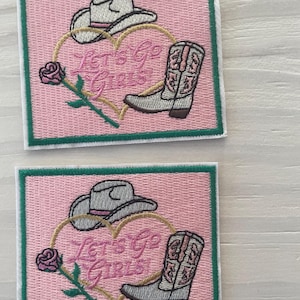 May include: Two pink and green embroidered patches with a heart, a cowboy hat, a cowboy boot, and the text "Let's Go Girls".