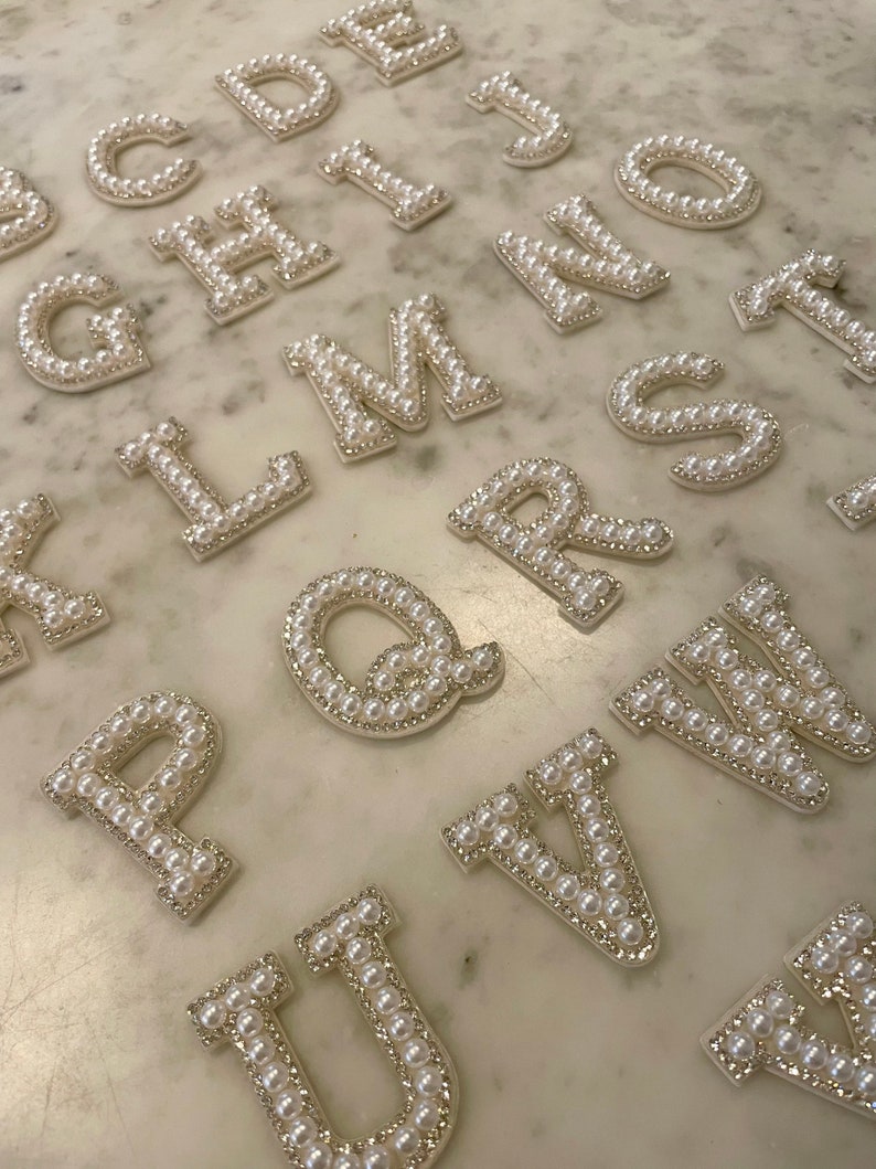 May include: A set of pearl-embellished letters, each letter is made of white fabric and covered in white pearls. The letters are arranged in alphabetical order, starting with A and ending with Z.