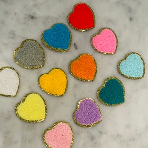 May include: A set of 12 felt heart patches in various colors, including red, blue, pink, orange, yellow, purple, gray, white, and teal. Each heart has a gold outline.