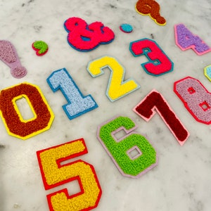 May include: A set of colorful felt patches with numbers 0-8 and the ampersand symbol. The patches are in various colors, including yellow, red, blue, green, and pink.