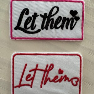 May include: Two rectangular embroidered patches. The top patch has a white background with a pink border and the words "Let them" in black script, with two black hearts. The bottom patch has a white background with a red border and the words "Let them" in red script, with a red heart.