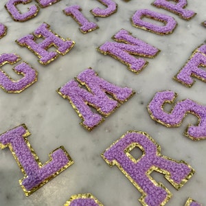 May include: Purple felt letters with gold glitter trim. The letters are in uppercase and include the letters A, B, C, D, E, F, G, H, I, J, K, L, M, N, O, P, Q, R, S, T, U, V, W, X, Y, and Z.