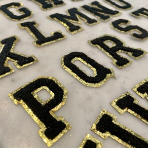 May include: Black felt letters with gold glitter trim. The letters are arranged in alphabetical order, starting with A and ending with Z.