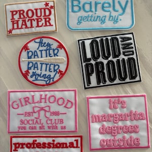 May include: A collection of embroidered patches with various phrases. The patches feature text like "PROUD HATER," "Barely getting by," "LOUD AND PROUD," and "It's margarita degrees outside." The patches are in various colors.