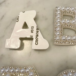 May include: White foam letters with pearl and rhinestone embellishments. The letters are A, B, E, and C. The letter A has a sticker on the back that says "CROWN #513".