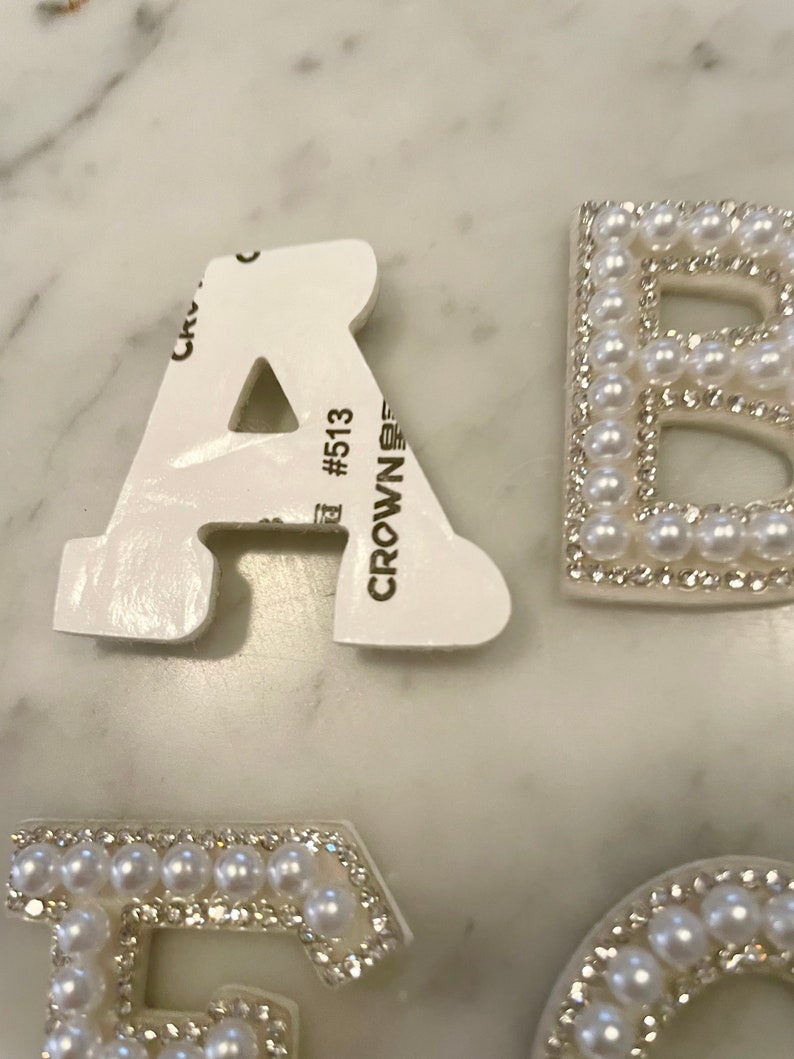 May include: White foam letters with pearl and rhinestone embellishments. The letters are A, B, E, and C. The letter A has a sticker on the back that says "CROWN #513".