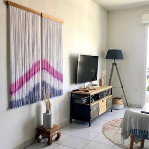 Puede incluir: Dos tapices de macramé blanco con un diseño de chevron rosa y azul. Los tapices están montados en barras de madera, añadiendo un toque bohemio a la decoración de la habitación.