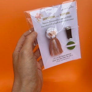 Peut inclure: Un diffuseur de parfum pour voiture pr&eacute;sent&eacute; dans un emballage plastique transparent. Le kit comprend un pompon blanc et beige, un clip noir et un cercle vert. Le texte sur la carte dit "DIFFUSEUR pour VOITURE".