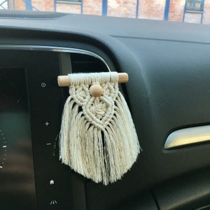 Può includere: Ciondolo per auto in macramè color crema con tassello e perla in legno. Il pezzo fatto a mano presenta nodi intricati e una frangia di fili pendenti con accenti dorati. Progettato per essere appeso allo specchietto retrovisore di un'auto.