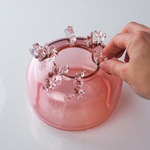 May include: A pink glass bowl with a unique design featuring clear glass accents around the rim. The bowl has a rounded shape and a smooth, glossy finish.