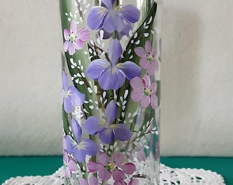 Puede incluir: Un jarrón cilíndrico alto de vidrio transparente con un diseño floral pintado a mano de lirios morados y pequeñas flores rosas con hojas verdes. El borde del jarrón está acentuado con una banda gruesa de vidrio azul cobalto sólido.