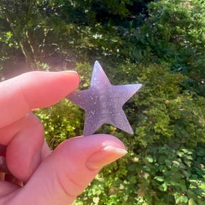 May include: A sparkly, iridescent purple star-shaped ornament. The star is made of a clear material with a glittery finish.