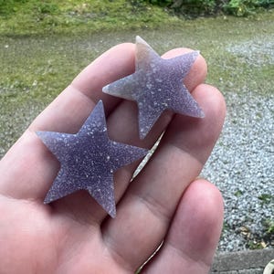 May include: Two purple star-shaped crystals with a sparkly finish.