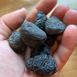 May include: A handful of dark grey, rough, and textured stones. The stones have a slightly metallic sheen and appear to be volcanic in origin.
