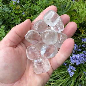 May include: A collection of clear quartz tumbled stones in various sizes. The stones are smooth and polished, with a translucent appearance.