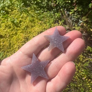 May include: Two purple star-shaped amethyst crystals. The crystals are smooth and have a sparkly texture.
