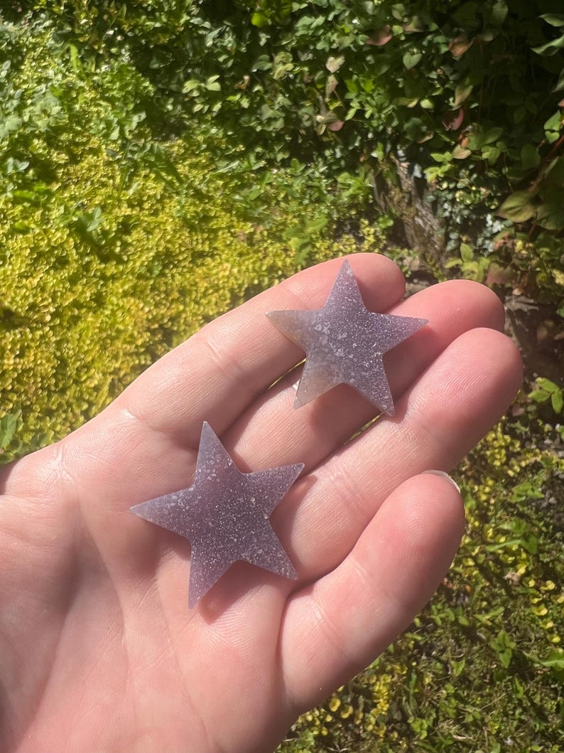 May include: Two purple star-shaped amethyst crystals. The crystals are smooth and have a sparkly texture.