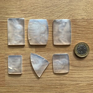 May include: Six clear, translucent, rectangular and triangular shaped pieces of plastic on a wood surface. A silver coin is also on the surface.