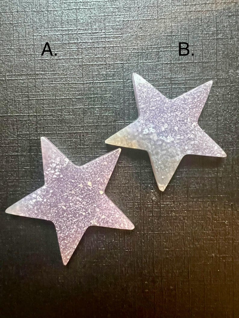 May include: Two iridescent purple glitter star-shaped ornaments with a textured surface. The stars are labeled "A." and "B."