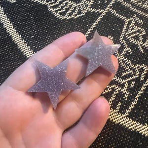 May include: Two purple glitter star-shaped resin earrings.