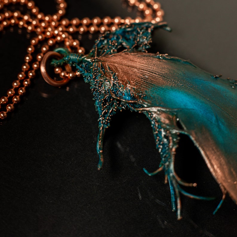 Puede incluir: Un collar de cadena de cobre con un gran colgante intrincado. El colgante est&aacute; hecho de metal y tiene un acabado turquesa y cobre. El colgante tiene la forma de una hoja con un dise&ntilde;o org&aacute;nico detallado.