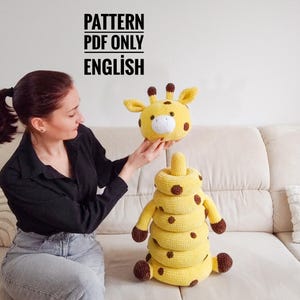 May include: A yellow and brown crochet giraffe stacking toy. The toy has a giraffe head and a body made of stacking rings. The text "PATTERN PDF ONLY ENGLISH" is visible in the image.