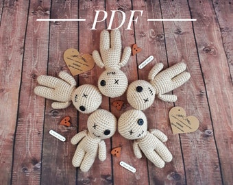 May include: A collection of six beige crochet dolls with black button eyes and stitched facial features, arranged on a wooden surface. The dolls have arms and legs, and are accompanied by wooden heart and button accents. The word "PDF" is written across the top.
