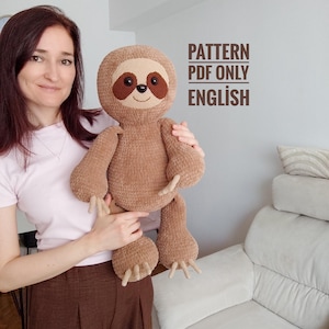 May include: A brown crocheted sloth plush toy with dark brown eye patches, black button eyes, and a stitched smile. The text PATTERN PDF ONLY ENGLISH is printed in brown letters on the wall next to the plush toy, indicating a digital file.