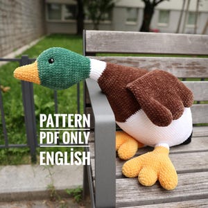 May include: A handmade plush duck with a green head, brown body, and yellow feet. The duck is sitting on a wooden bench. The text "PATTERN PDF ONLY ENGLISH" is visible.