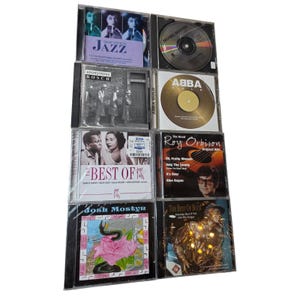 Puede incluir: Una colección de álbumes en CD en estuches transparentes, que presentan varios géneros musicales. Las portadas de los álbumes presentan texto e imágenes, como "Great Voices in Jazz", "ABBA Gold" y "The Best of Buck".