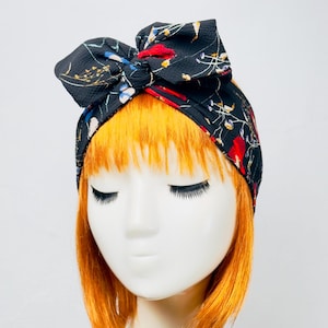 Puede incluir: Una diadema negra con estampado floral en tonos rojos, azules y amarillos. La diadema está atada en un lazo en la parte superior de la cabeza.