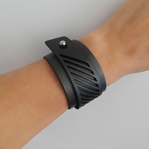 Peut inclure: Un bracelet en cuir noir avec un motif géométrique et un fermoir en métal argenté.