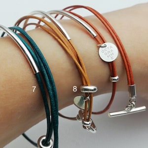 Könnte beinhalten: Drei Lederarmbänder mit silbernen Akzenten. Das obere Armband hat einen silbernen Anhänger mit dem Text "OCTA GRAMME". Das mittlere Armband hat einen silbernen Herzanhänger. Das untere Armband hat eine silberne Perle.
